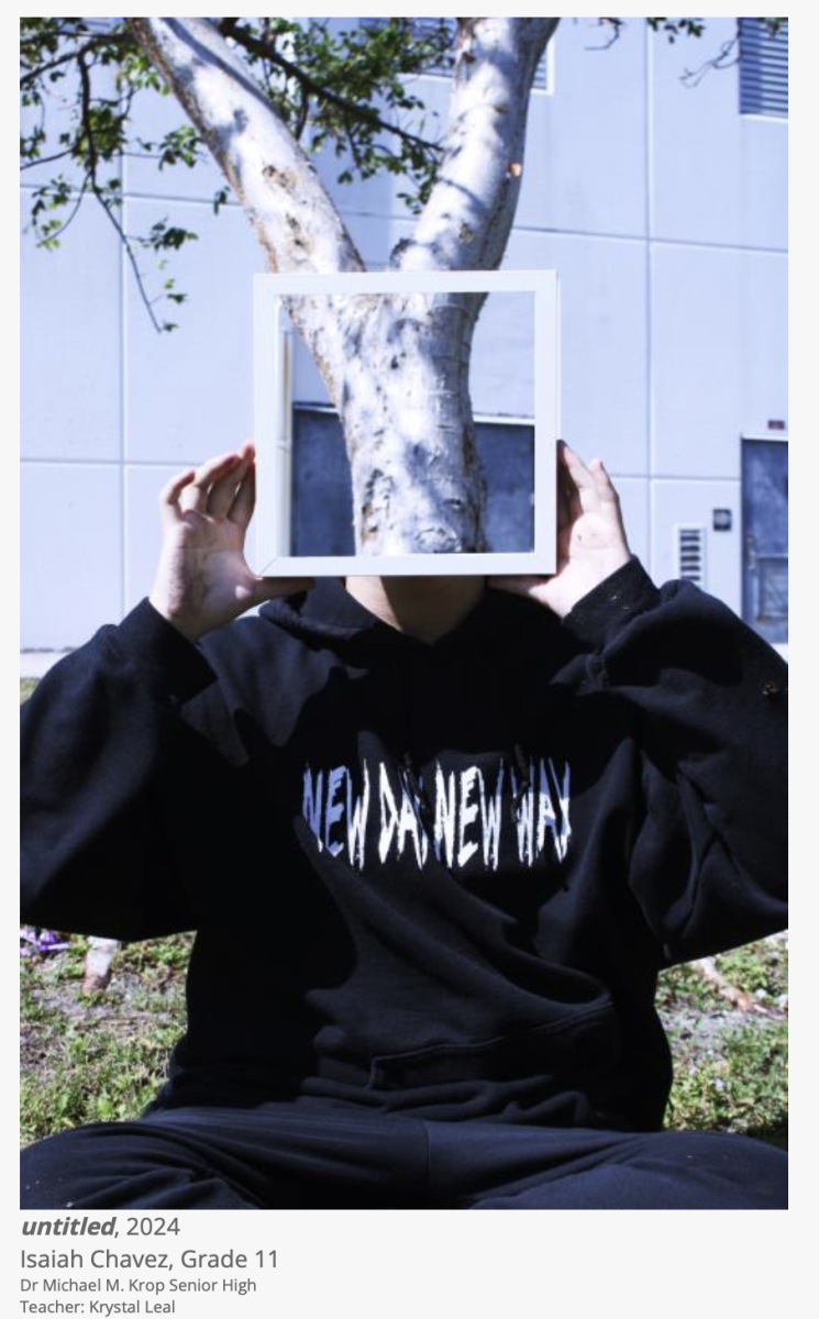 A student holds up a border showing the tree behind the students face. This photograph is being exhibited at a gallery at Miami International Airport (MIA).