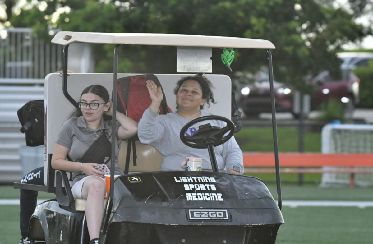 RIDIN' AROUND: Medical Trainer Juliana Edwards, driving a student to the sidelines of a night game at Ives Estates Park.